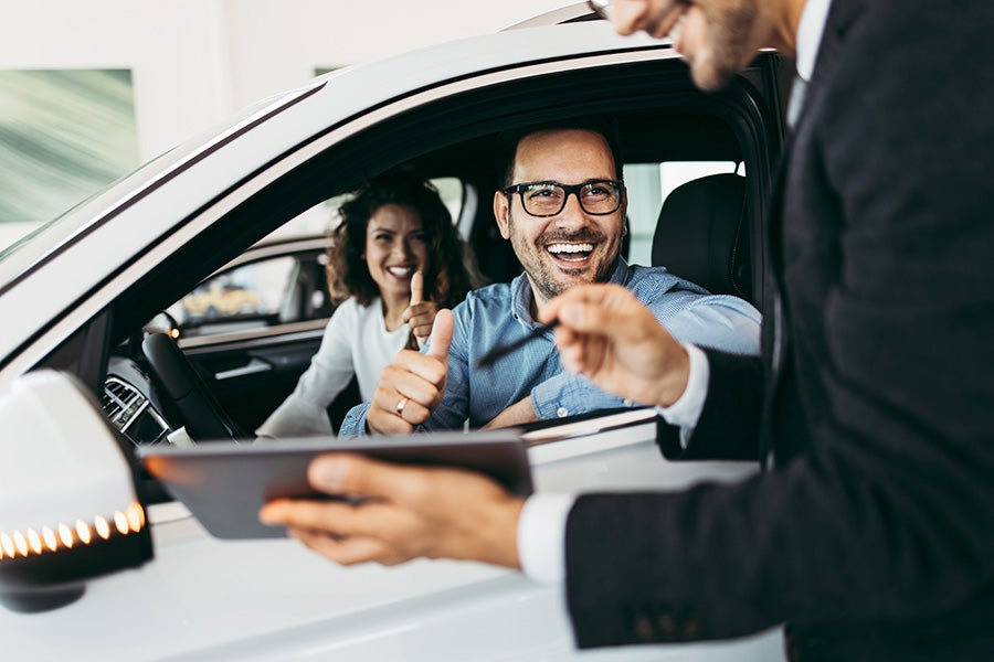 A happy man in a car going over a tablet with a salesperson
